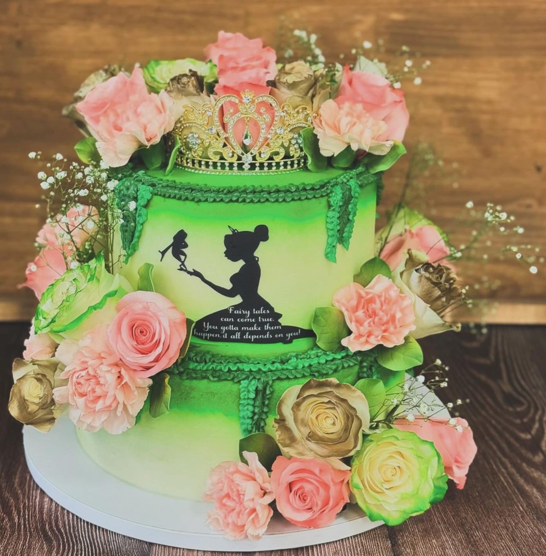 A green tiered cake with roses and a princess and frog silhouette. 