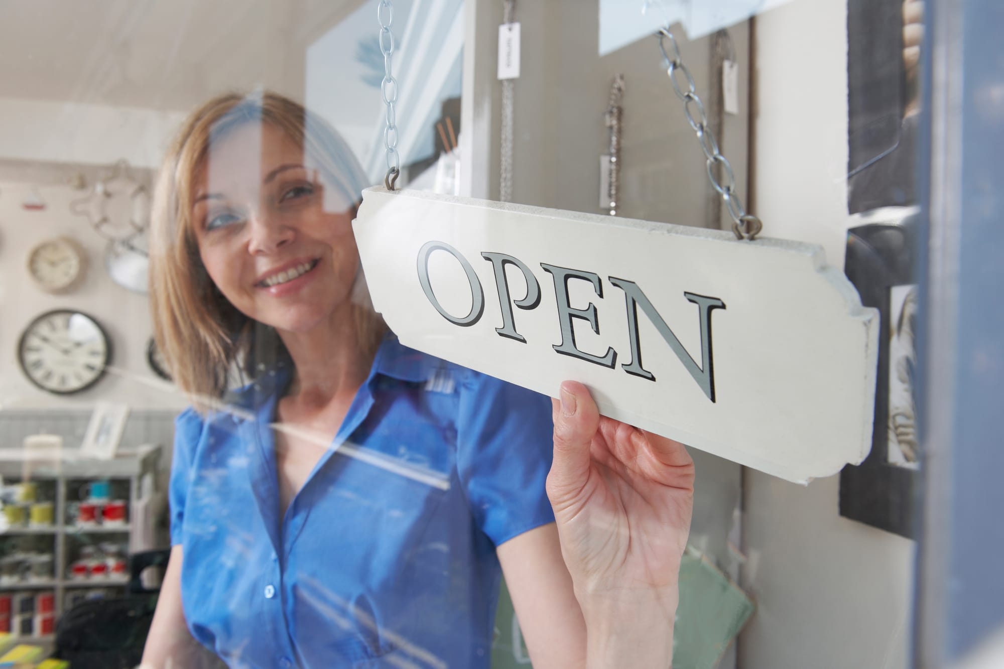 Business woman shop owner tuning an open sign on the front business door.