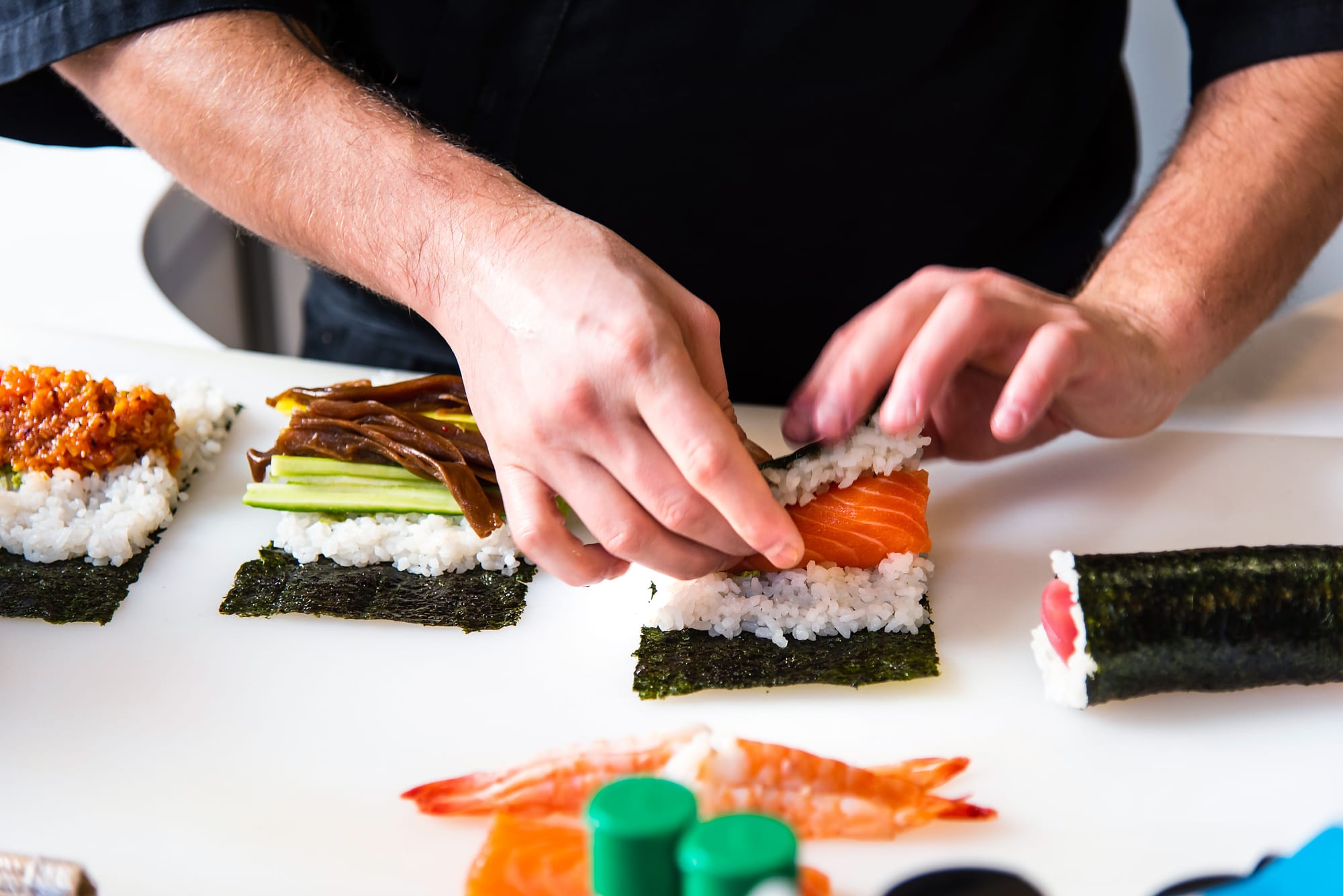 Sushi chef rolling maki ingredients in seaweed for a single salmon roll.