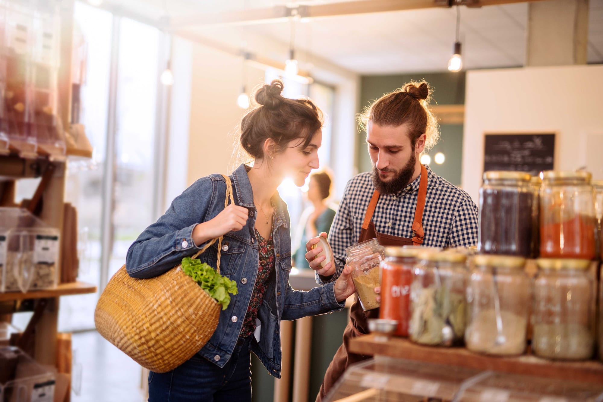 A shop owner shows a customer a food product inside a jar