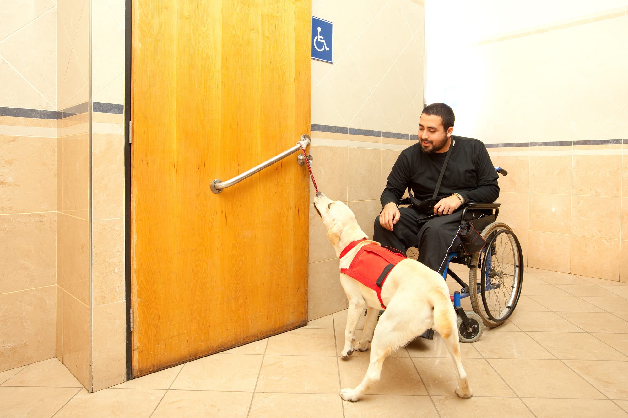 Service dog opening a bathroom door for its handler in a restaurant.