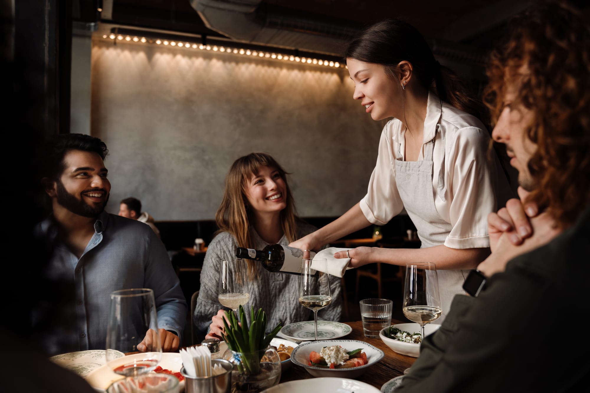 Waitress pouring wine for guests at restaurant