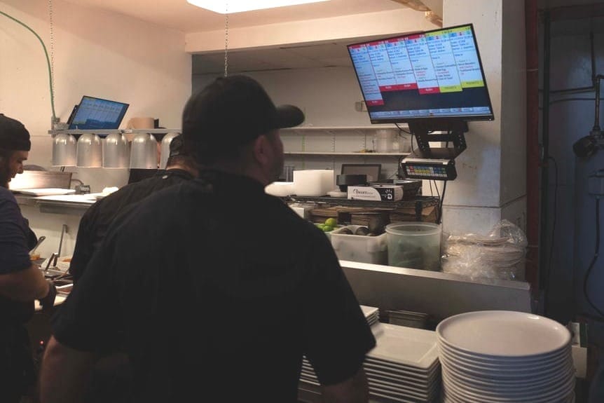 Cooks in a kitchen looking at orders on a kitchen display system.